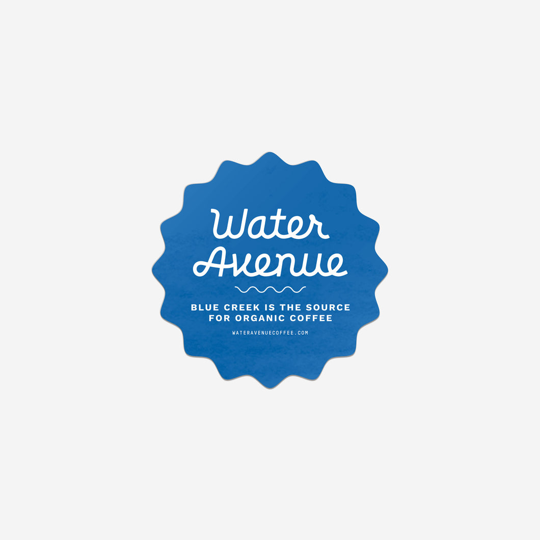 Water Avenue - Blue Creek is the source for organic coffee. Blue, wavy-edged circular sticker with white detailing.